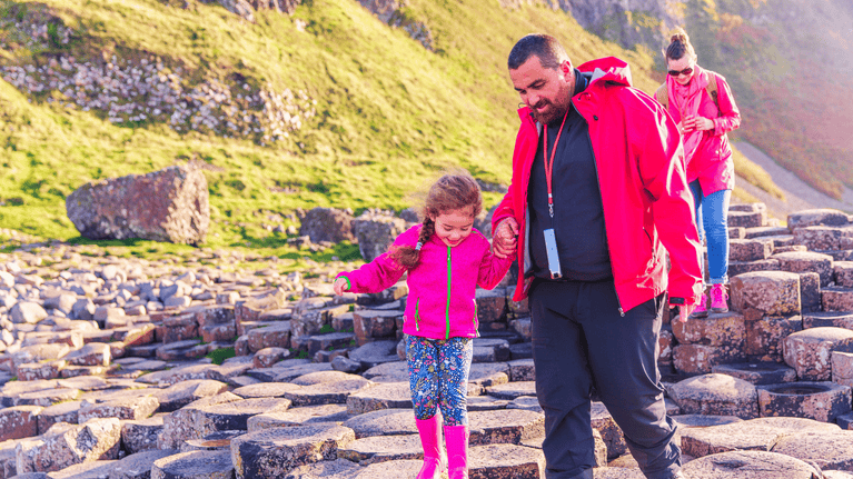 A family walking hand-in-hand across the basalt columns of the Giant's Causeway on a spring, sunny day